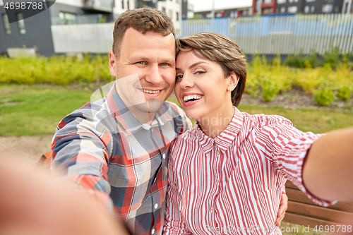 Image of happy couple in park taking selfie outdoors