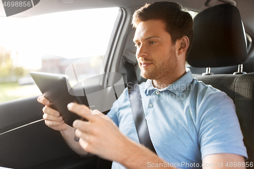 Image of male passenger using tablet computer in taxi car