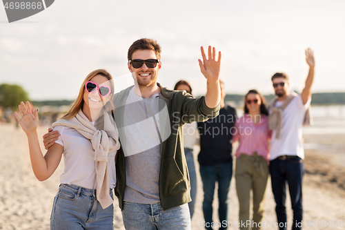 Image of happy couple with friends waving hands on beach