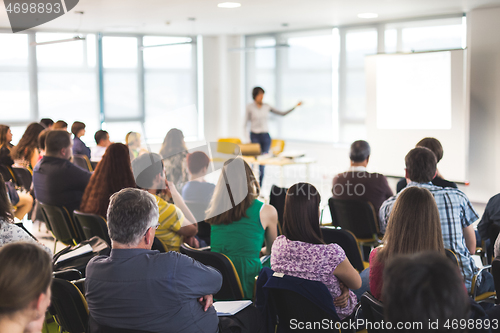 Image of Speaker giving a talk in conference hall at business meeting event. Rear view of unrecognizable people in audience at the conference hall.