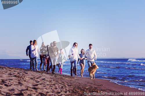 Image of Group of friends running on beach during autumn day