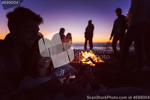 Image of Couple enjoying bonfire with friends on beach