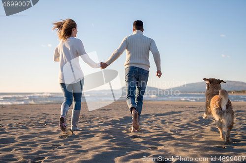 Image of couple with dog having fun on beach on autmun day