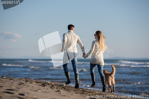 Image of couple with dog having fun on beach on autmun day