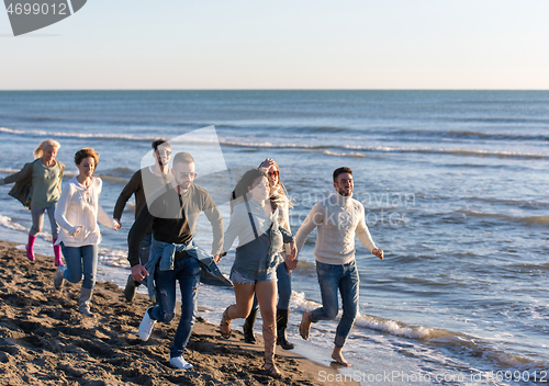 Image of Group of friends running on beach during autumn day