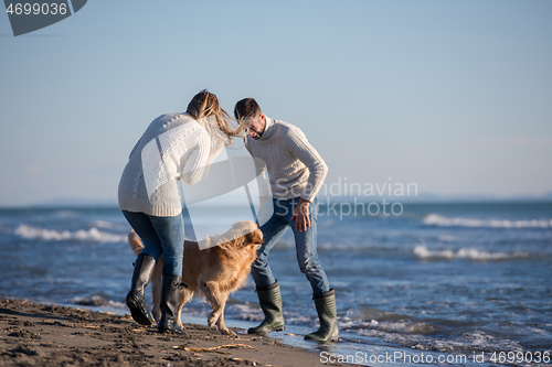 Image of couple with dog having fun on beach on autmun day