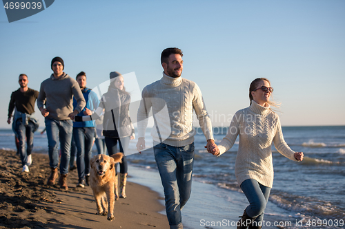 Image of Group of friends running on beach during autumn day