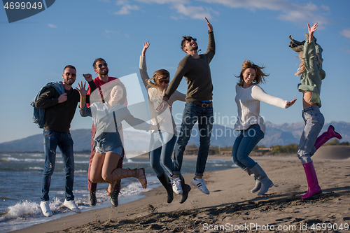 Image of young friends jumping together at autumn beach
