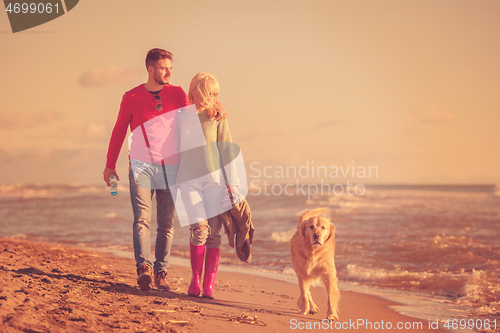 Image of couple with dog having fun on beach on autmun day