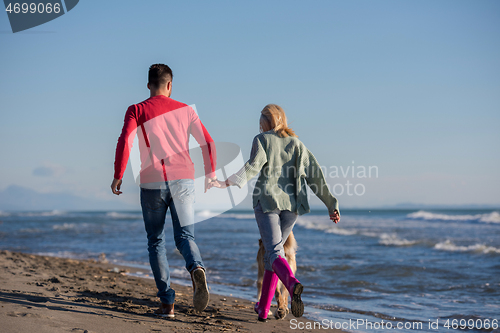 Image of couple with dog having fun on beach on autmun day