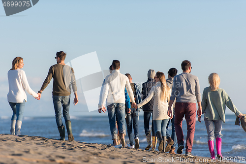 Image of Group of friends running on beach during autumn day