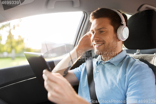 Image of passenger in headphones with tablet pc in taxi car