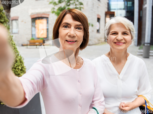 Image of old women with shopping bags taking selfie in city