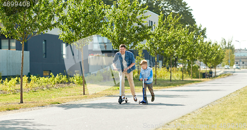 Image of father and little son riding scooters in city