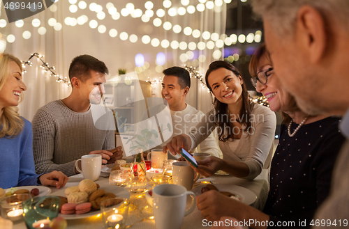 Image of happy family with smartphone at tea party at home