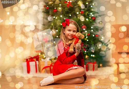 Image of girl in red dress hugging teddy bear at home