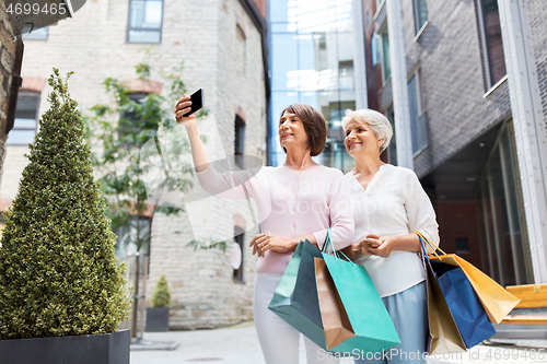 Image of old women with shopping bags taking selfie in city