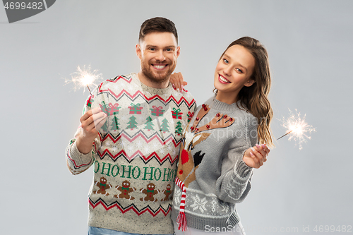 Image of happy couple in christmas sweaters with sparklers