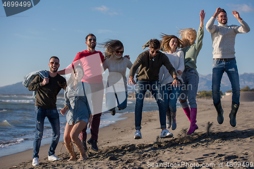 Image of young friends jumping together at autumn beach