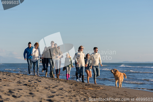 Image of Group of friends running on beach during autumn day