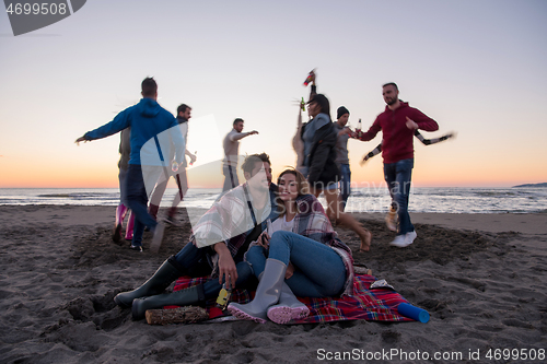 Image of Couple enjoying with friends at sunset on the beach