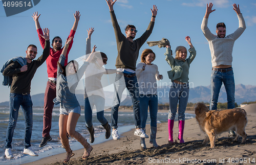 Image of young friends jumping together at autumn beach