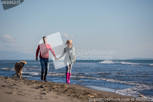 Image of couple with dog having fun on beach on autmun day