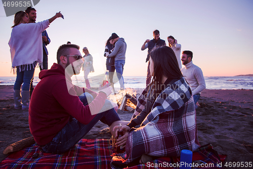 Image of Couple enjoying with friends at sunset on the beach