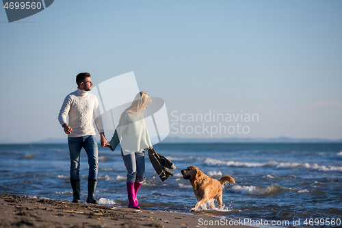 Image of couple with dog having fun on beach on autmun day