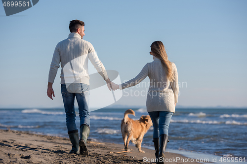 Image of couple with dog having fun on beach on autmun day