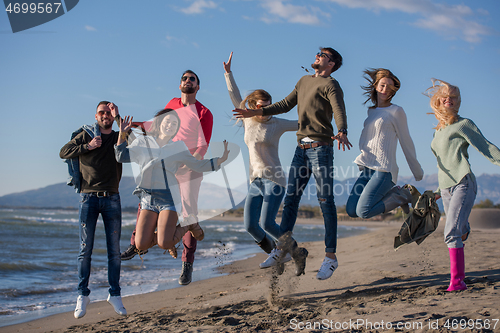 Image of young friends jumping together at autumn beach