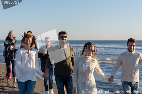 Image of Group of friends running on beach during autumn day