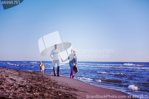 Image of couple with dog having fun on beach on autmun day
