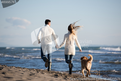 Image of couple with dog having fun on beach on autmun day