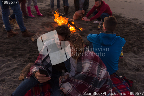 Image of Couple enjoying bonfire with friends on beach