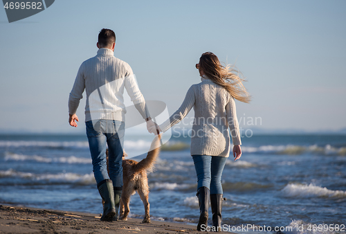 Image of couple with dog having fun on beach on autmun day