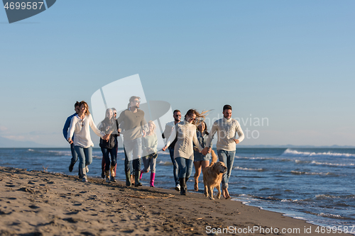 Image of Group of friends running on beach during autumn day