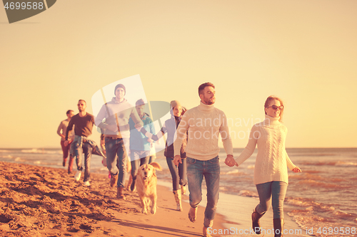 Image of Group of friends running on beach during autumn day