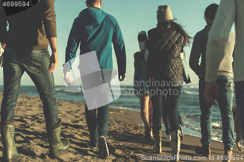 Image of Group of friends running on beach during autumn day