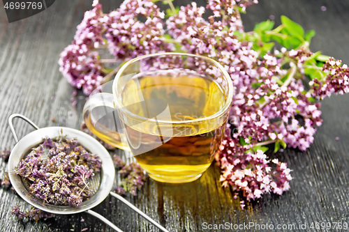 Image of Tea of oregano in cup with strainer on wooden board