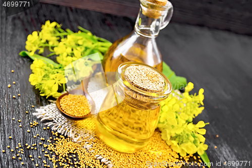 Image of Oil mustard in jar and decanter with flower on dark board