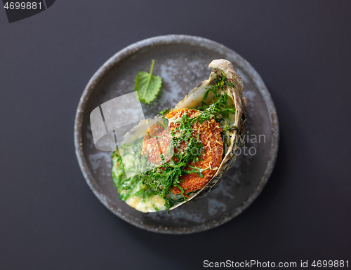 Image of baked oyster with toasted bread and greens on grey plate, top vi