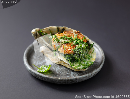 Image of baked oyster with toasted bread and greens on grey plate