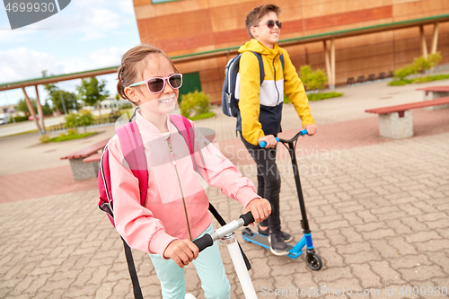 Image of happy school children with backpacks and scooters