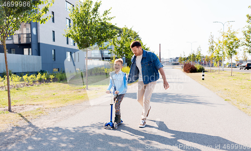 Image of happy father and little son riding scooter in city