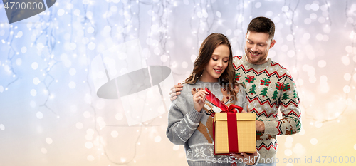 Image of happy couple in christmas sweaters with gift box