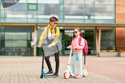 Image of happy school children with backpacks and scooters