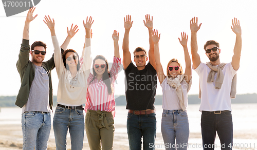 Image of happy friends waving hands on beach in summer
