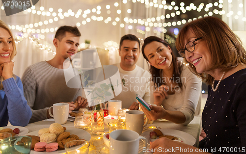 Image of happy family with smartphone at tea party at home