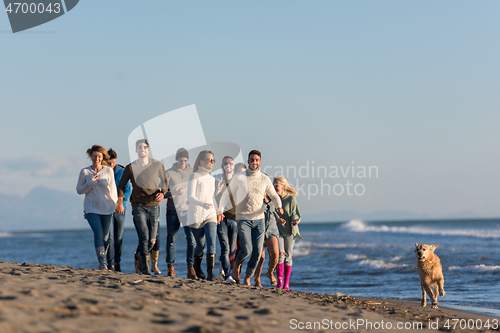 Image of Group of friends running on beach during autumn day